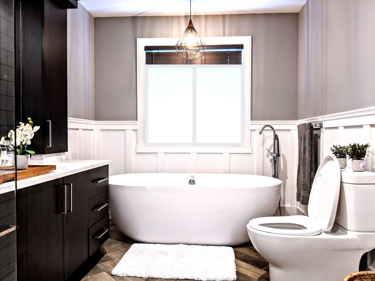 Salle de bain rénovée avec baignoire autoportante sous une fenêtre lumineuse, lambris à planches et couvre-joints et meuble-lavabo en bois foncé